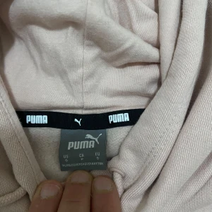 Rosa  hoodie från Puma - Säljer en snygg beige hoodie från Puma med klassisk logga i vitt på bröstet. Hoodien har en stor ficka framtill och justerbar huva med dragsko. Perfekt för en avslappnad stil.