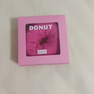 Rosa strumpor i donut-förpackning från Soxo - Snygga rosa strumpor från Soxo, förpackade i en rolig donut-liknande låda. Perfekt som present eller för att liva upp din strumplåda. Strumporna har ett lekfullt mönster med färgglada detaljer.
