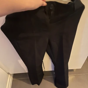 Svarta byxor från RYVLS - Snygga svarta bootcut byxor från RYVLS med låg midja och knappar framtill. Perfekta för en stilren look. Passar bra till både vardag och mer uppklädda tillfällen.