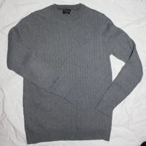 Grå stickad tröja från Massimo Dutti - Säljer en stilren grå stickad tröja från Massimo Dutti. Tröjan har ett diskret kabelstickat mönster och långa ärmar.