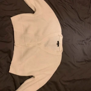 Vit ribbad kofta  - Säljer en stilren vit ribbad kofta. Koftan har långa ärmar och knappar framtill, perfekt för lager-på-lager under kyligare dagar. En klassisk och mångsidig del i garderoben.