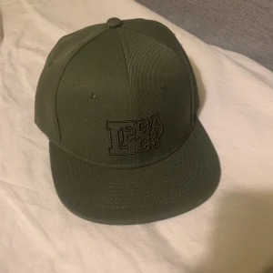 Olivgrön Laidback Keps - Snygg olivgrön keps från Legacy med broderad text framtill. Kepsen har en klassisk design med platt skärm och justerbar passform. Perfekt för en avslappnad stil.