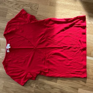 Röd ribbad topp - Säljer en snygg röd ribbad topp med korta ärmar. Perfekt för en färgglad look. Toppen har en enkel design som gör den lätt att matcha med olika outfits.