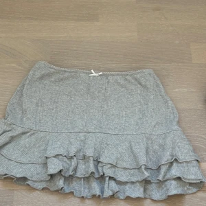 Grå volangkjol från Out From Under - Säljer en söt grå volangkjol från urban outfitters. Kjolen har en ribbad struktur och flera lager volanger som ger en lekfull look. Perfekt för att styla med en enkel topp eller stickad tröja. 🩶