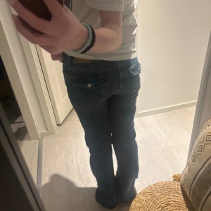 Blå bootcut jeans från 157 - Snygga blå bootcut jeans med intressanta fickor från 157. De är inte använda jättemycket men har blivit trasiga längst ner för att dem varit lite för långa. På ena benet syns det rätt så mycket på nära håll, men inte när man har på sig de, se på sista sidan. På andra benet är det knappt några defekter. 