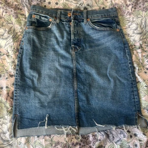 Jeanskjol med slitna detaljer - Snygg jeanskjol i klassisk blå denim med slitna detaljer och rå kant. Kjolen har en normal passform och knappar framtill. Perfekt för en avslappnad stil. Två fickor fram och två fickor bak. Storlek M från lager 157