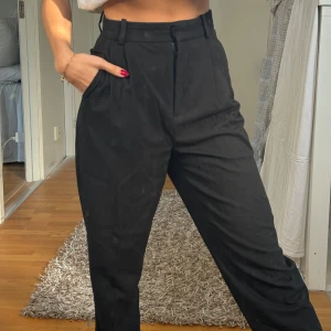 Svarta kostymbyxor - Snygga svarta kostymbyxor med hög midja och dragkedja framtill. Byxorna har en klassisk rak passform och är perfekta för en stilren look. De är tillverkade i ett bekvämt material som ger en elegant känsla.