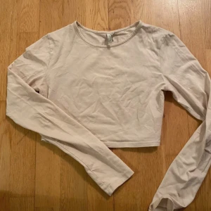 Beige croppad långärmad topp från Nelly - Säljer en beige croppad långärmad topp från Nelly. Perfekt för en stilren look med sin enkla design och mjuka material. Passar bra till både jeans och kjol. 🧡