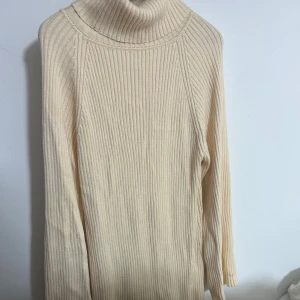 Beige ribbad poloklänning - Säljer en stilren beige polo klänning med ribbad struktur. Klänningen har långa ärmar och en hög polokrage som ger en mysig känsla. Den är midi lång 