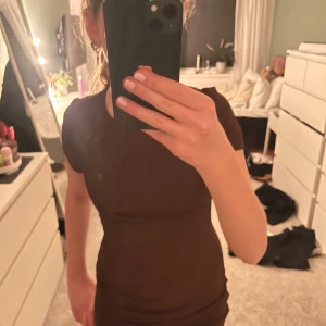 Brun klänning med rynkdetalj - Säljer en snygg brun klänning med rynkdetalj längs sidan. Klänningen har korta ärmar och en tight passform som framhäver figuren. Perfekt för en stilren look!