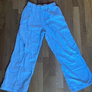 Randiga byxor från Lindex - Säljer ett par bekväma randiga byxor från Lindex i ljusblått och vitt. Byxorna har en loose passform och är tillverkade i ett lätt och luftigt material, perfekt för varma dagar.