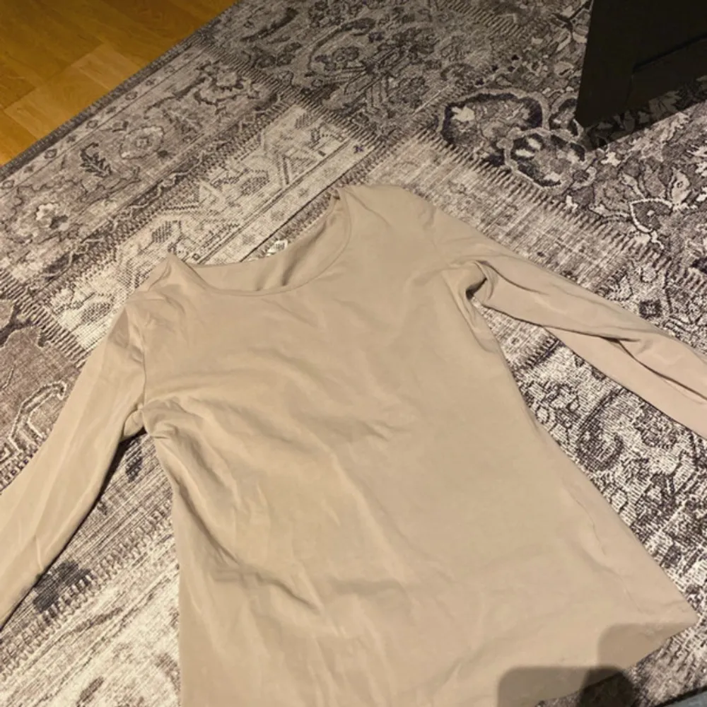 Säljer en stilren beige långärmad topp i mjukt material. Perfekt för en enkel och avslappnad look. Passar bra till både jeans och kjol.. Neuletakit & Villapaidat.