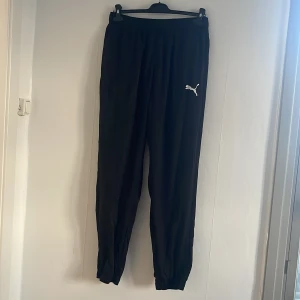 Svarta träningsbyxor från Puma - Säljer ett par svarta träningsbyxor från Puma med elastisk midja och logga på benet. Perfekta för en avslappnad stil. Tillverkade i ett mjukt och bekvämt material.