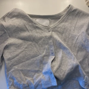 Grå ribbad kofta från 157 - Säljer en grå kofta ifrån Lager 157 i storlek 150. Den har knappar framtill och långa ärmar. Köpte för ca 1år sedan, men är knappt använd och inga tecken på användning. Priset kan diskuteras🩶