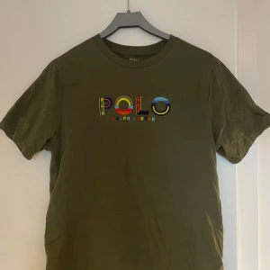 Olivgrön t-shirt från Ralph Lauren - Säljer en olivgrön t-shirt från Ralph Lauren med färgglatt broderat POLO-märke på bröstet. T-shirten är kortärmad och tillverkad i mjuk bomull. Perfekt för en avslappnad stil. Aldrig använd. Storlek Xl för barn så skulle säga Small 