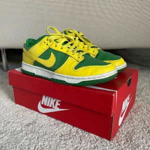 Nike Dunk Low Retro i grönt och gult - Snygga Nike Dunk Low Retro sneakers i en fräsch kombination av grönt och gult. Skorna har en klassisk design med snörning och en bekväm passform. Perfekta för att ge din stil en färgklick. Kvitto finns!
