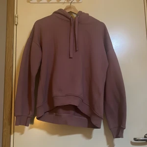 Rosa hoodie - Säljer en mysig rosa hoodie med luva och dragsko. Tröjan har långa ärmar och ribbade muddar vid ärmslut och nederkant. Perfekt för en avslappnad stil.