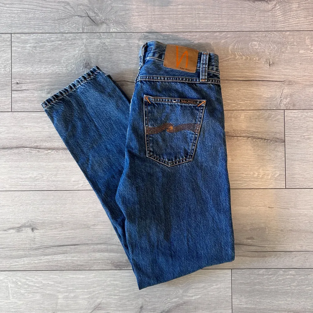 Säljer ett par klassiska blå jeans från Nudie Jeans med snygg broderad detalj på bakfickan. Jeansen har en normal passform och är tillverkade i slitstarkt denim. Perfekta för en avslappnad stil.. Farkut & Housut.