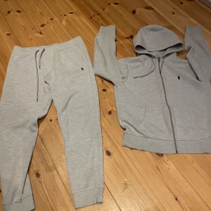 Ralph Lauren tracksuit  - Säljer ett set med grå hoodie och matchande byxor från Ralph Lauren. Hoodien har dragkedja och snörning i huvan, medan byxorna har en bekväm resårmidja med snörning. Båda plaggen har den klassiska Ralph Lauren-loggan broderad i svart. Perfekt för en avslappnad stil. Ralph lauren dress i ny skick i strl M byxor strl l 