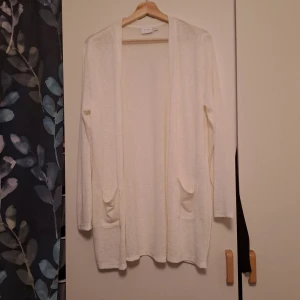Vit kofta från Vero Moda - Säljer en stilren vit kofta från Vero Moda. Den har långa ärmar och två praktiska fickor framtill. Perfekt för lager-på-lager under kyligare dagar. Passar till många olika outfits!