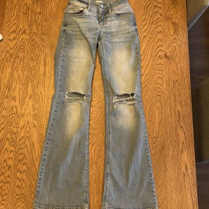 Blå bootcut jeans från Nelly - Snygga blå bootcut jeans från Nelly med slitna detaljer på knäna. Jeansen har låg midja och klassiska femficksdesign med knappar. Något slitna nere vid fötterna, annars bra skick. Nypris 700