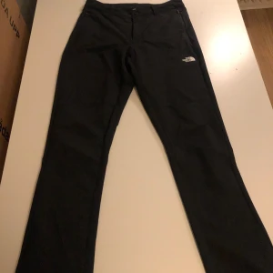 Svarta byxor från The North Face - Snygga svarta byxor från The North Face med en diskret logga på låret. Perfekta för en stilren och bekväm look. Byxorna har en rak passform och är tillverkade i ett slitstarkt material.
