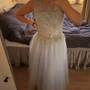 Elegant ljusblå klänning med spetsdetaljer - Säljer en fantastisk ljusblå/ljusgråa långklänning med vackra spetsdetaljer och pärlor. Klänningen har en ärmlös design och en elegant, transparent övre del med blommönster. Perfekt till balen🤍 Specialbeställda mått men är som en normal S och är 163 cm! (Har tyvärr inte kvar de exakta måtten då jag använde klänning för 3 år sen) nypris 3500 säljer för 1500🤍