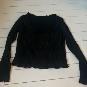 Svart glittrig topp - Snygg svart topp med glittriga detaljer och långärmad design. Toppen har en v-ringad hals och är perfekt för en kväll ute. Materialet är lätt och bekvämt. Det är dubbel lager på framsidan och den yttersta delens V ringning har lossnat i sömmen