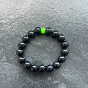 Svart pärlarmband med grön detalj - Snyggt svart armband med glansiga pärlor och en unik grön pärla som accent. Perfekt för att ge en subtil färgklick till din outfit.