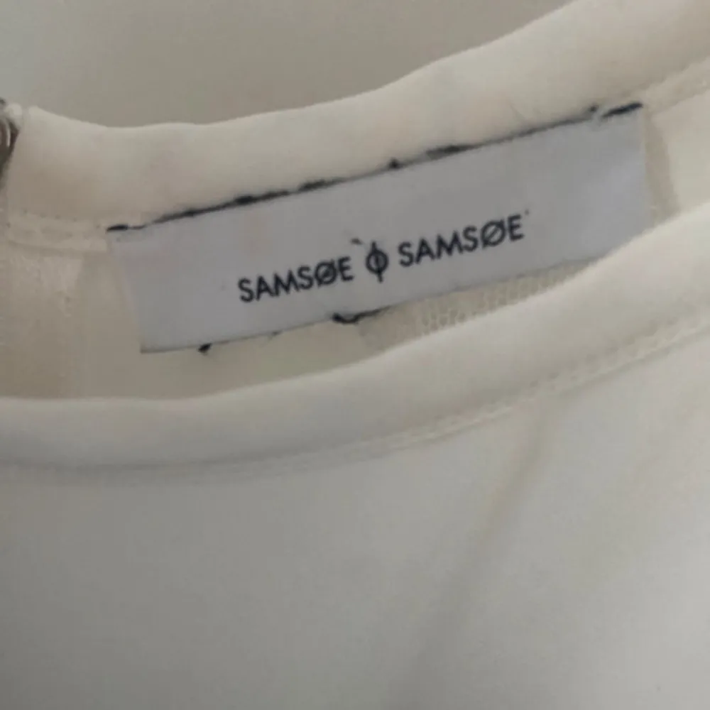 Elegant vit blus från Samsøe Samsøe med transparenta detaljer på ärmarna och dragkedja i ryggen. Blusen har korta ärmar och en rund halsringning, perfekt för en stilren look. Storlek S/M. Yläosat.