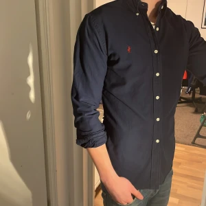 Ralph Lauren Skjorta - Tja säljer en Ralph lauren skjorta i färgen marinblå och i storlek S passar 170-180 cm ungefär. Nypris 1595 KR mitt pris 225 KR. En liten defekt (bild 5) skrapmärke som inte går igenom och knappt syns. Skriv vid frågor eller funderingar.