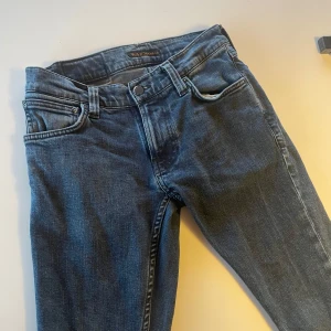 Blå jeans från Nudie Jeans - Snygga blå jeans från Nudie Jeans med klassisk femficksdesign och knappgylf. Jeansen har en stilren look med diskreta sömmar och en bekväm passform. Perfekta för en avslappnad stil. I storleken 27/30