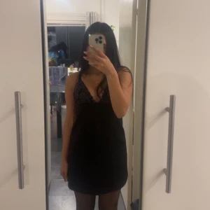 Svart klänning med spetsdetaljer - Snygg svart kortklänning med spetsdetaljer och djup v-ringning. Perfekt för en kväll ute. Klänningen har smala axelband och en figurnära passform. Köpt för 400kr från Zara och bara använd en gång för nyår. Pris kan diskuteras.