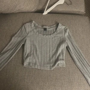 Grå ribbad croppad tröja från Shein - Säljer en stilren grå ribbad tröja från Shein. Den e liten i storleken.Den är croppad och har långa ärmar, perfekt för en trendig look. Passar bra till både jeans och kjol. Perfekt för höst och vår!