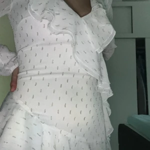 Studentklänning  - Säljer en söt vit klänning med volanger och diskret mönster. Klänningen har långa ärmar och en v-ringad design. Perfekt för en stilren look och perfekt för studenten!