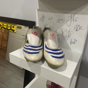 Adidas f30 - Säljer ett par vita och blå fotbollsskor från Adidas med klassisk design och mönstrade detaljer. Skorna har en robust sula med dobbar för bra grepp på planen. Perfekta för fotbollsentusiaster som vill ha stil och funktionalitet.