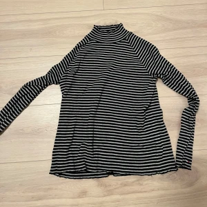 Svart och vit randig polotröja - Säljer en stilren svart och vit randig polotröja med långa ärmar. Perfekt för en avslappnad och trendig look. Tröjan har en klassisk passform och är gjord i ett mjukt material för extra komfort.