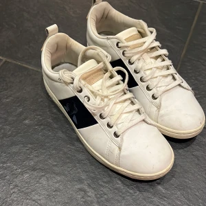 Vita sneakers  - Snygga vita sneakers med mörkblå detalj på sidan och snörning. Perfekta för en avslappnad stil. Märket har en diskret logga på hälen och sidan. Använda några gånger men ändå i gott skick. 