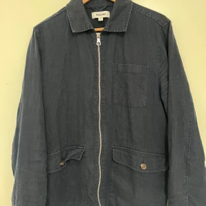 Mörkblå overshirt från Kappahl - Snygg mörkblå jacka från Kappahl med dragkedja framtill och två fickor med knappar. Jackan har en klassisk krage och en bröstficka. Perfekt för en stilren look. Storlek S men sitter mer som M