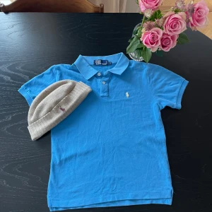 Ralph Lauren piké 10-12 - Detta är en Ralph Laurent piké, huvudfärgen är blå och logan är gul. Skicken av tröjan är bra och använd 2-3 gånger. Nyköppris var cirka 699 kr. Den är storlek 10-12 alltså 146-152 cm