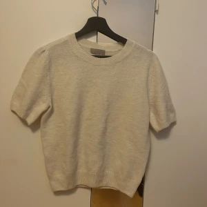 Vit kortärmad stickad tröja från H&M - Säljer en vit stickad tröja från H&M med korta ärmar. Tröjan är i ett mjukt material och har ribbade kanter vid ärmslut och nederkant. Har aldrig använt då den inte passar.