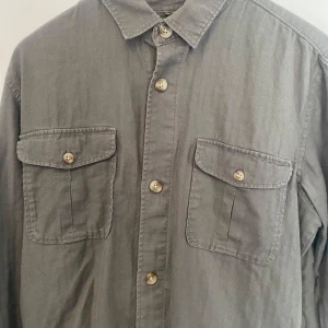 Grå overshirt med fickor - Säljer en fet skjorta/over shirt i storlek M från dressman. Snygg grön färg perfekt till våren. Skicket är 7/10