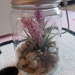 Gullig decorativ upplysbar blommburk - Skapa en varm och mysig stämning med den här unika ljusburk! En glasburk med metallock, fylld med dekorativa stenar, lila fejk blommor och en vacker ljusslinga som ger ett mjukt sken. Perfekt som heminredning, nattlampa eller present. Köpt i butik Normal. Funkar som nytt, inga problem med den. 