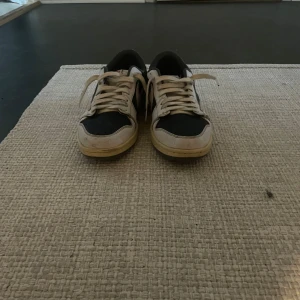 Nike sneakers med Travis Scott-design - Säljer ett par unika Nike sneakers i samarbete med Travis Scott. Skorna har en stilren design med svart och vit färgkombination samt ikoniska detaljer. Perfekta för sneaker-entusiaster som vill ha något speciellt i sin samling.