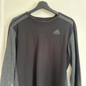 Svartgrå långärmad tröja från Adidas - Säljer en stilren svart och grå långärmad tröja från Adidas. Tröjan har en diskret logga på bröstet och är perfekt för både träning och vardag. Den är tillverkad i ett mjukt och bekvämt material.