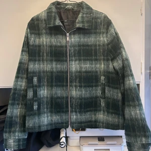 Grön rutig jacka från Asos Design - Snygg grön rutig jacka från Asos Design med dragkedja framtill. Jackan har en klassisk krage och långa ärmar. Perfekt för höst och vår med sitt stilrena mönster och bekväma passform.