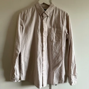 Beige skjorta från S.C.W. - Säljer en stilren beige skjorta från S.C.W. i regular fit. Skjortan har långa ärmar och en klassisk krage med knappar framtill. Perfekt för en avslappnad men ändå uppklädd look.