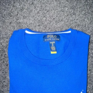 Blå tröja från Ralph Lauren - Snygg blå tröja från Ralph Lauren med klassisk design. Tröjan har en rund halsringning och är prydd med den ikoniska logotypen i vitt på bröstet. Perfekt för en stilren look.