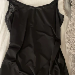 Svart linne - Elegant svart linne med smala axelband och en stilren design. Perfekt för en chic och minimalistisk look. Materialet ger en slät och glansig finish.