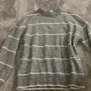 Grå vitrandig tröja från H&M - Mysig grå tröja från H&M med vita ränder. Tröjan är långärmad och har en ribbad krage samt ribbade muddar vid ärmslut och nederkant. Perfekt för kyligare dagar.